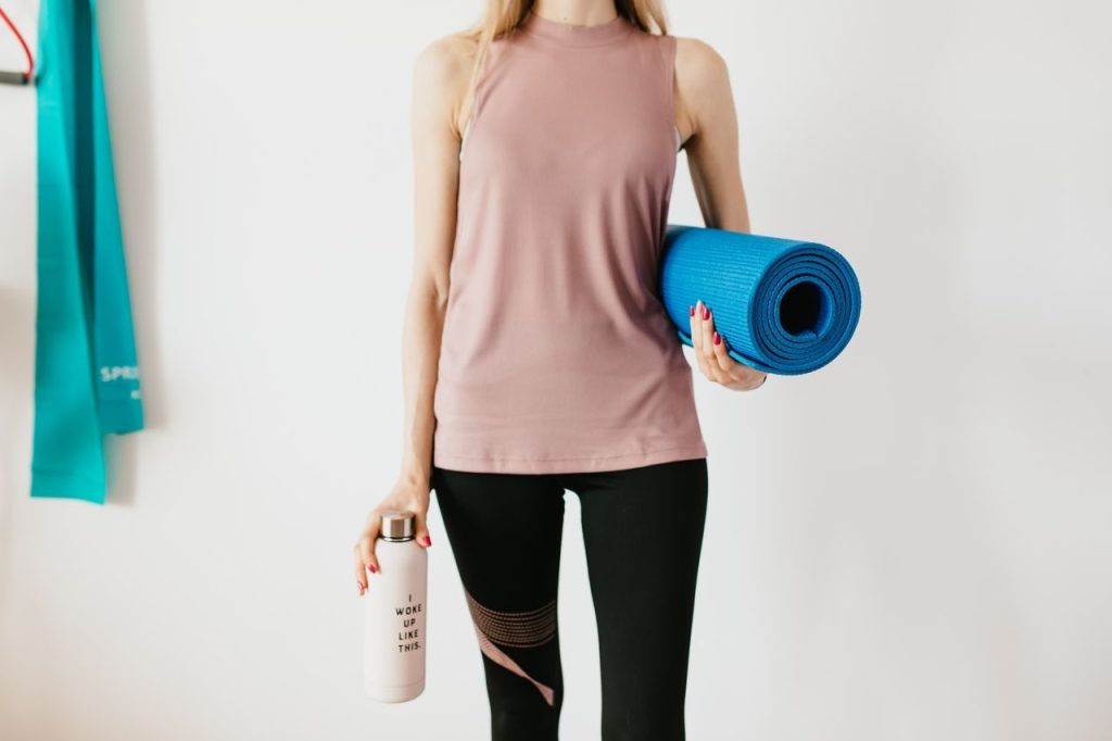 An unidentifiable person carrying a rolled mat and water bottle
